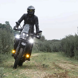 Rider on a motorcycle equipped with bright DENALI D3 LED driving lights on a dirt trail.