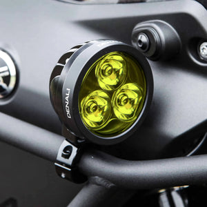 DENALI D3 round LED motorcycle driving light with yellow lens mounted on a black handlebar.