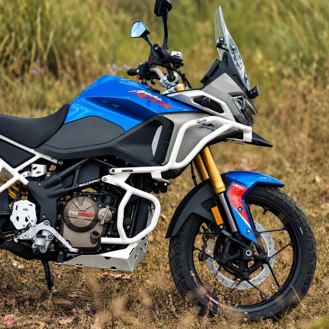 White Raptor crash guard set installed on a blue TVS Apache RTX 300 motorcycle in a grassy field