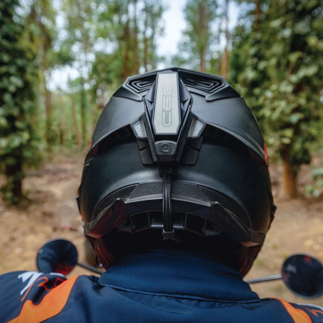 Motodrift BluArmor C60 Bluetooth mesh intercom mounted on a black motorcycle helmet, viewed from behind on a forest road