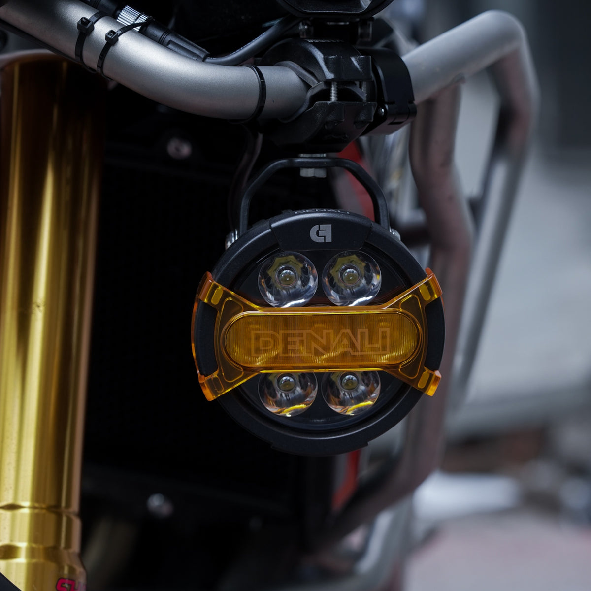 Motodrift DENALI D7 PRO auxiliary LED light pod with an amber modular X-Lens mounted on a motorcycle crash bar
