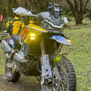 Motodrift Future Eyes Z4 auxiliary LED lights mounted on a muddy adventure motorcycle in a forest setting