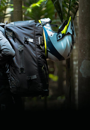 Motodrift Rynox Navigator 50L black Cordura tail bag worn by a rider with a motorcycle helmet in a forest setting