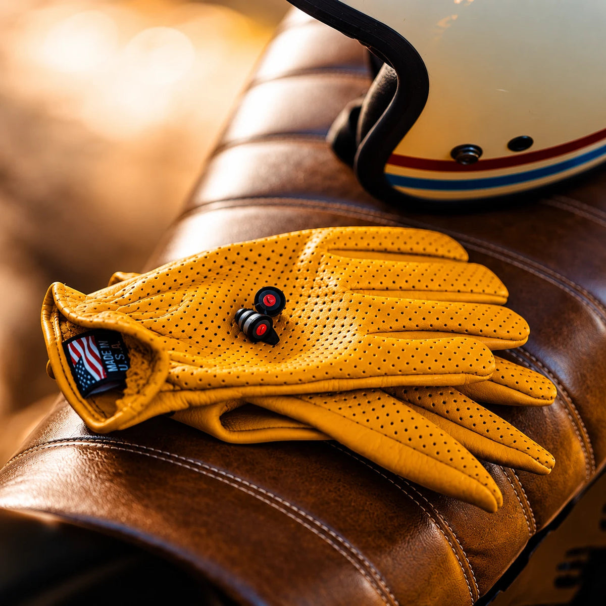 Pinlock motorcycle earplugs with precision filters resting on yellow perforated leather riding gloves.