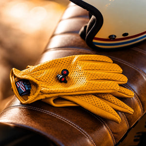 Pinlock motorcycle earplugs with precision filters resting on yellow perforated leather riding gloves.
