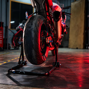 RKTECH Uni Paddock Stand in glossy black supporting a motorcycle rear wheel in a workshop setting