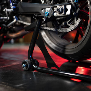 RKTECH Uni Paddock Stand in glossy black supporting a motorcycle rear swingarm for maintenance