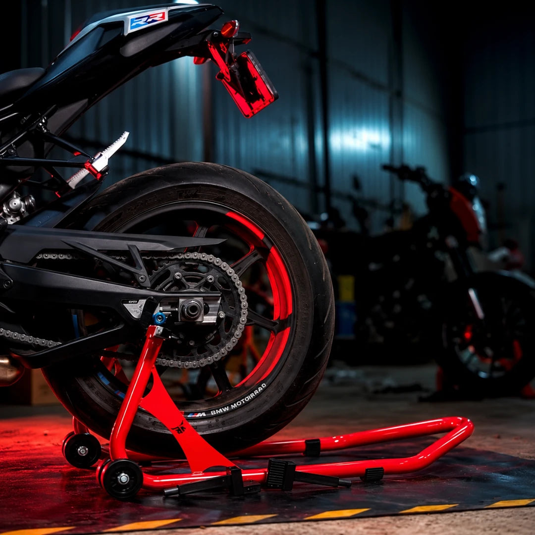 RKTECH Uni Paddock Stand in cosmic red supporting a motorcycle rear wheel in a workshop setting