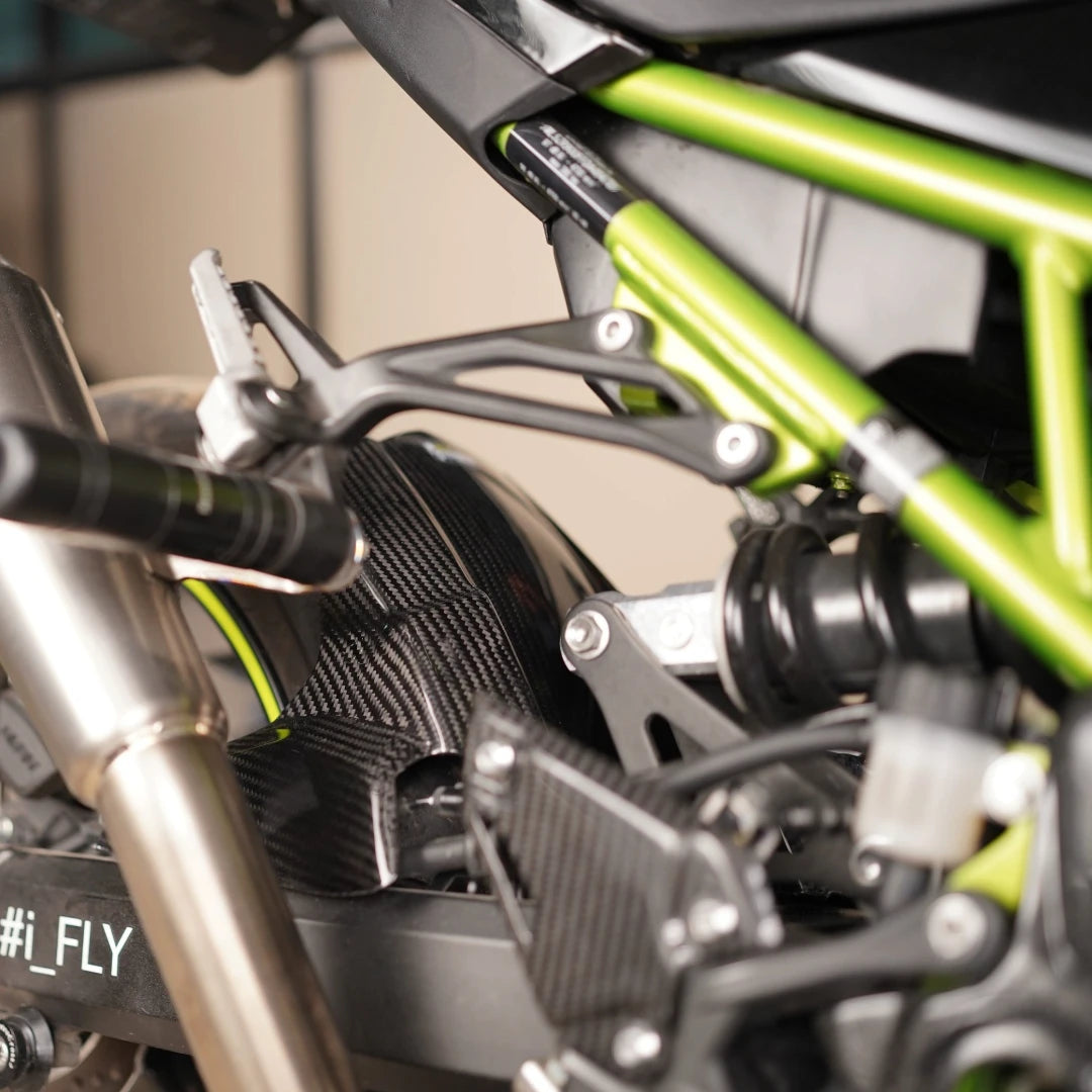 Carbon fiber rear hugger with chain guard in twill gloss finish installed on a Kawasaki Z900 motorcycle.
